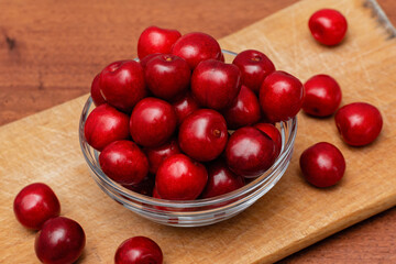 fresh black cherries in glass plate on wooden board on a wooden background