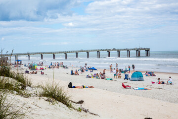 St Augustine, Florid, the beach just south of St Augustine with people sun bathing and swimming.  A fishing pier in the background. - obrazy, fototapety, plakaty