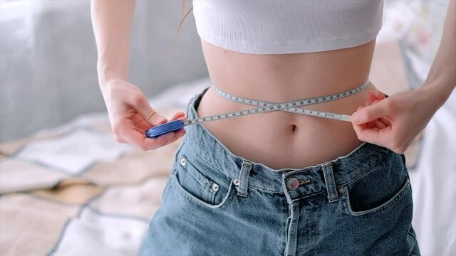 Slim woman measuring her waist's size with tape measure on white background. Successful weight loss. Slim fit concept.