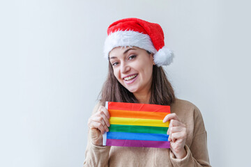 Beautiful lesbian girl in red Santa Claus hat with LGBT rainbow flag isolated on white background looking happy and excited. Young woman Gay Pride portrait. Happy Christmas and New Year holidays