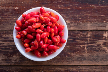 Fresh berries of wild rose in a white plate on a wooden table.