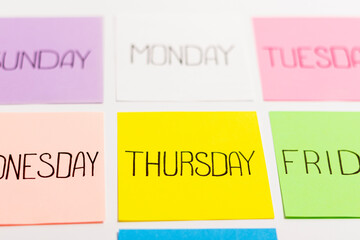 Sheets of paper of different colors are arranged in a straight tile. Each piece of paper has the name of one day of the week written on it.