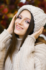 A beautiful girl walks in the fresh air in autumn. A smiling girl holds her hands on a knitted hat. A young woman enjoys the autumn weather