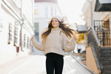A happy girl in a warm sweater and hat runs through the autumn city. She develops hair in the wind