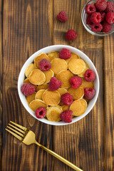 Top view of mini pancakes with raspberries in the white bowl on the wooden table. Location vertical.