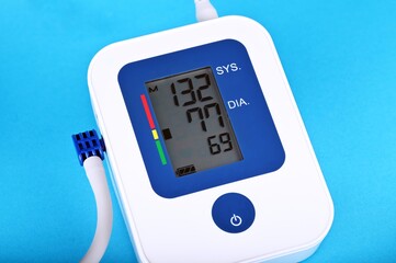 Digital blood pressure monitor on a blue background, close-up, shows high blood pressure