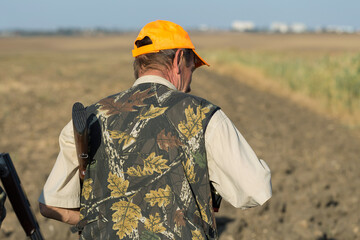 Duck hunter with shotgun walking through a meadow.