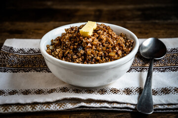 Buckwheat porridge with butter, in a white ceramic bowl, metal horse, kitchen napkin on a wooden table. Homemade food preparation.