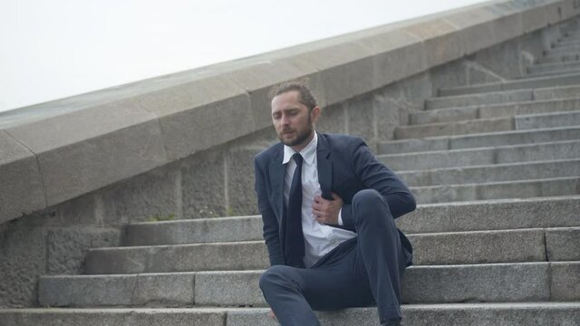 Young overworked businessman walking down stairs and having heart attack. Camera approaches to ill Caucasian man with heart failure because of overworking. Health care concept.