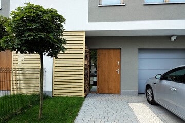 Entrance to a modern terraced house with green lawn, maple tree and car parked outside