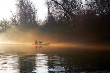 Kayaking in winter at sunrise in a foggy haze in the Danube river. A man and a woman row in a two-person kayak
