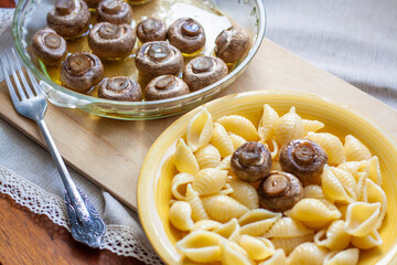 Baked mushrooms in a glass dish on the table, pasta shells with mushrooms in a plate, fork