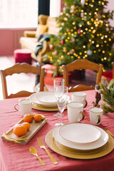 White plates, champagne glasses, tangerines in the serving of a festive dinner for Christmas, Christmas eve against the background of Christmas tree lights