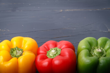 Three raw peppers.
Three raw peppers -Red, green and yellow- positioned at the bottom on a dark gray wooden background. Photograph with space to add text.