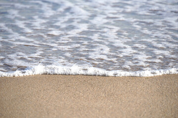 Sea water with wite foam and sand on the shore, selective focus