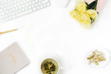 Flat lay women's office desk. Female workspace with a laptop, a bouquet of yellow peony-shaped tulips, accessories, a Cup of green tea on a white background. Top view female background copy space. 