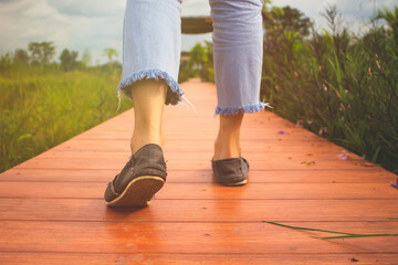 Close-up of walking woman feet in shoes on wooden bridge. Walking relax on walkway with sunlight, sunset.
