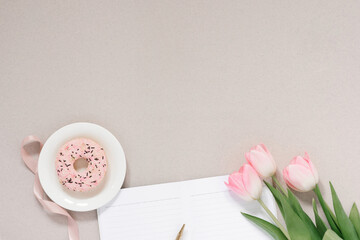 Obraz na płótnie Canvas Trendy stylish banner for a female blogger: pink donut, pink tulips and an open Notepad with a clean page on a coffee background with copy space
