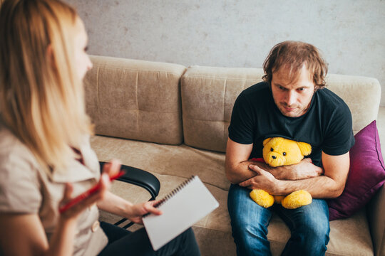 A woman psychologist provides psychological assistance to an adult man with a childhood psychological trauma - holds a teddy bear in arms