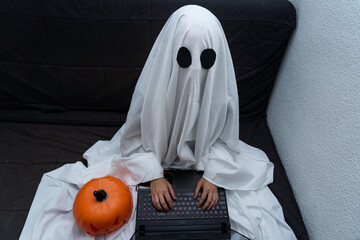 Ghost working from home on his computer sitting on the couch with a pumpkin
