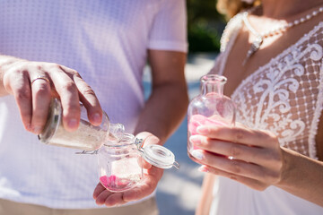 Close up view of bride and groom filling color sand into the jar at the wedding sand ceremony on the paradise beach, Punta Cana, Dominican Republic