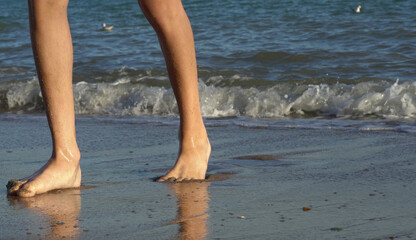 Human feet and sea waves on the shore, selective focus