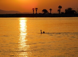 Man swimming in the golden sunset, near the shore of Glyfada, Greece
