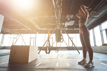 Prepering for workout. Side view of strong athletic woman in sportswear adjusting hair while standing at industrial gym, exercising with trx fitness straps
