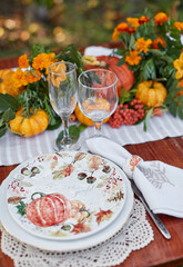 Table setting on a rustic farmhouse country table with white and orange mini pumpkins, and crystal glasses for Thanksgiving Day or Halloween.