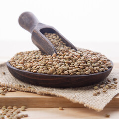 Raw lentils on wooden plate and wooden spoon, on light wood base. close-up view.