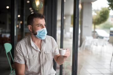 Man with surgical mask drinks coffee and looks out the window