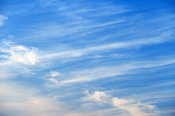 Blue sky covered with thin white clouds, a light yellow glow of the afternoon sun