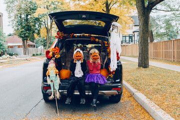 Trick or trunk. Children celebrating Halloween in trunk of car. Boy and girl with red pumpkins celebrating traditional October holiday outdoors. Social distance during coronavirus covid-19. - 382218027