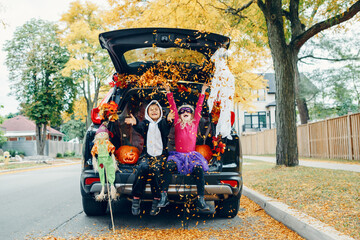 Trick or trunk. Children celebrating Halloween in trunk of car. Boy and girl with red pumpkins celebrating traditional October holiday outdoors. Social distance during coronavirus covid-19. - 382218239