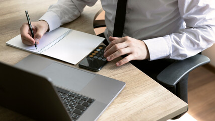 Closeup man hand working on wooden table at the office with laptop, mobile phone, pen and notebook. Banner.