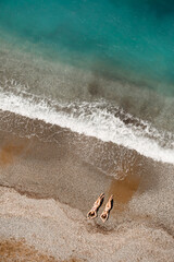 Aerial view of a woman in the Mediterranean Sea in Turkey. Beautiful summer landscape with a girl, clear azure water, waves and sandy beach on a sunny day. Top view from a flying drone.