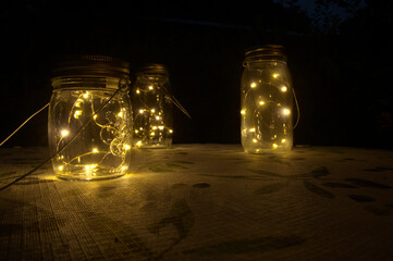 LED lamps in jars on garden table at night