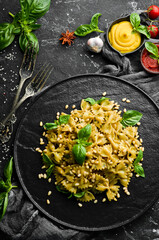 Farfalle pasta with pesto sauce and basil in a black stone plate. Top view. Free space for your text.