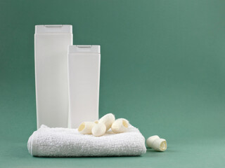 Two white bottles of shampoo, soft towel and silkworm cocoons on a green background.
