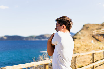 Fototapeta na wymiar Young sportsman stretching arms outdoors while looking at the horizon with the sea to the side.