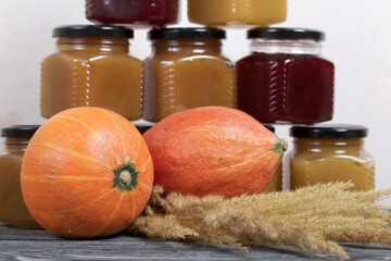 Jam in jars. Nearby is a pumpkin and a bouquet of dry grass with spikelets. On black pine boards.