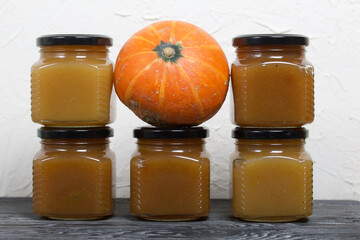 Jam in jars. There is a pumpkin nearby. On black pine boards.