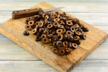 Freshly rinsed canned sliced black olives with kitchen knife on wooden cutting board