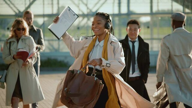 African american successful woman dances on the street celebrating day of employment listening music in headphones. Excited businesswoman going to work. - Powered by Adobe