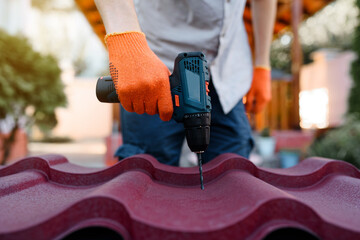 Close up of contractor hands in protective gloves are drilling with electric drill a metal tile...