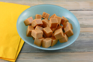 Caramel candy squares in blue bowl with two yellow napkins
