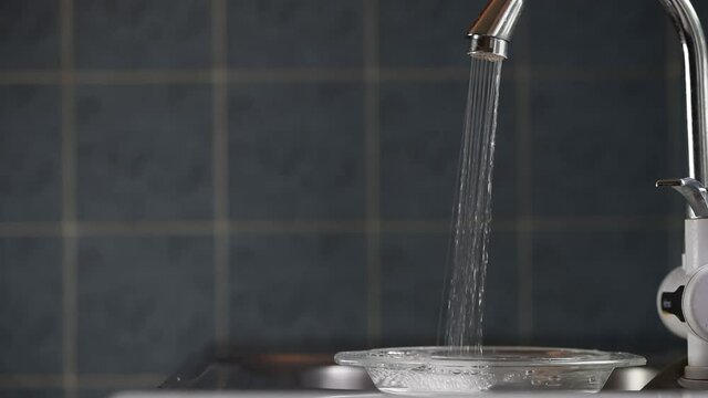 Mans hand opens the faucet in kitchen sink, water leaking from the tap