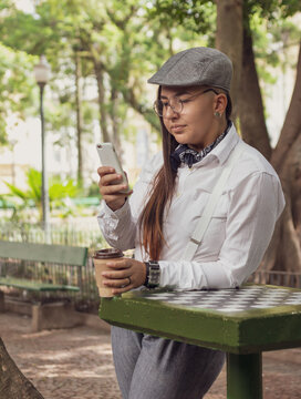 Serious vintage woman with cup of coffeet exting and typing on the mobile smart phone Outside in park and woods. Network, messaging, internet, lifestyle concept.