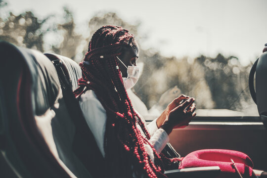 A Black Woman In A Virus Protective Face Mask And With Long Braided Hair Of Red Color Is Sitting On A Leather Seat Of A Regular Intercity Bus And Watching An Online Show Using Her Smartphone