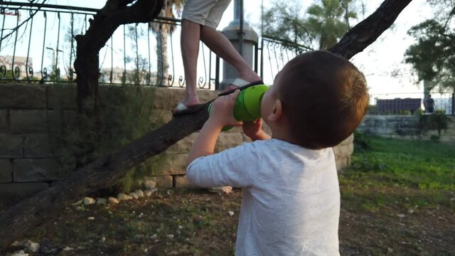 Cute baby boy drinking water and looking dady climbing on the tree. High quality 4k footage